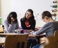 Eine Frau sitzt mit zwei Kindern an einem Tisch. Diese lernen.